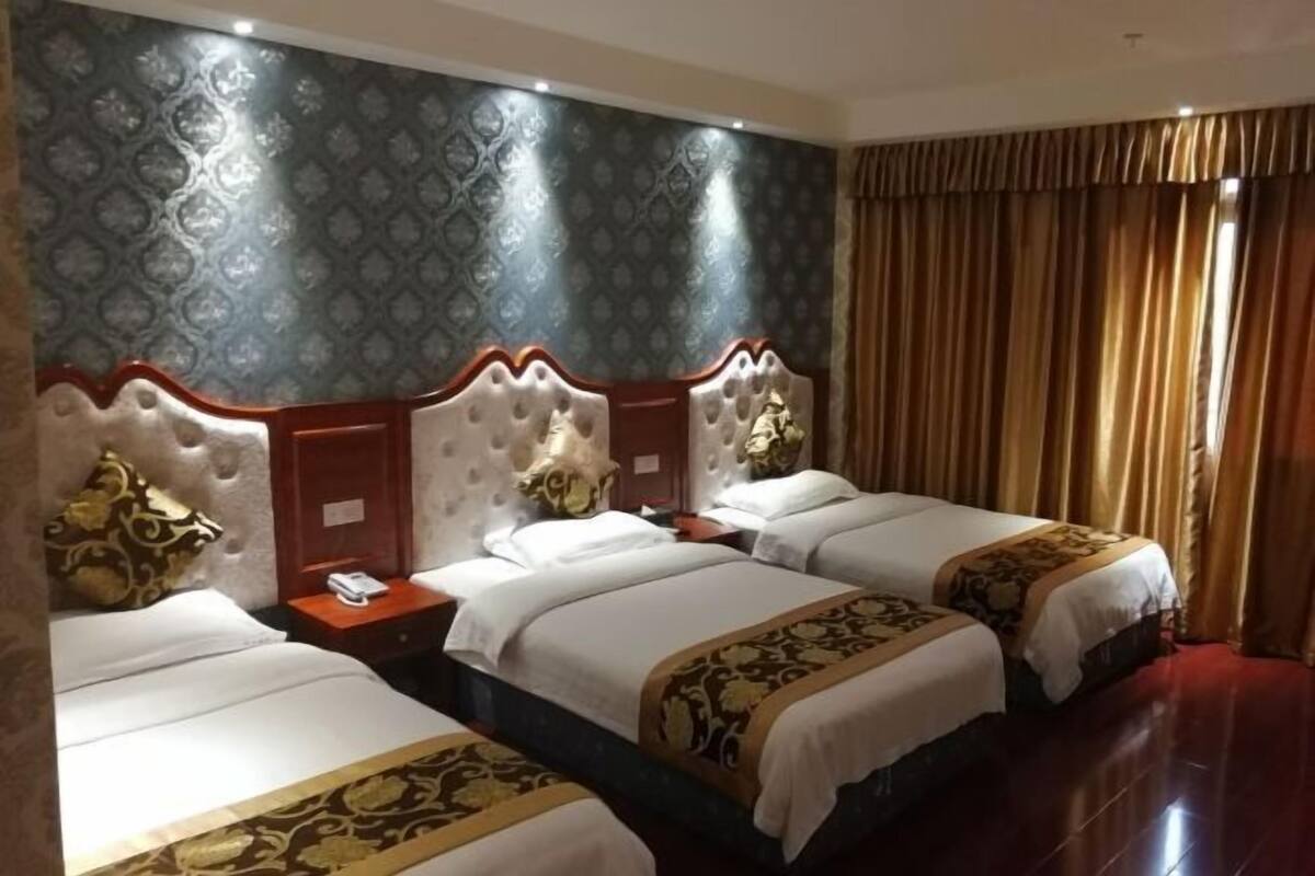 Een hotelkamer met drie bedden, een behang met patroon en een gordijn.