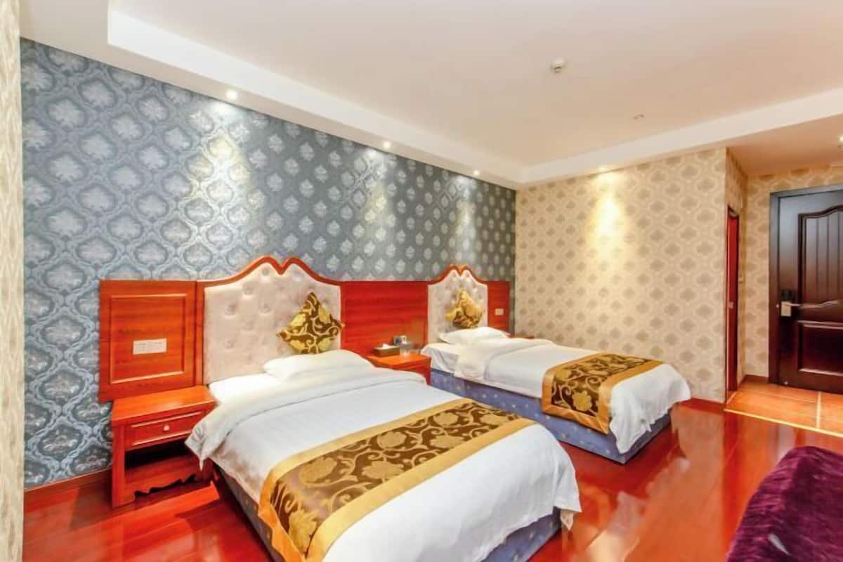 Een hotelkamer met twee bedden, houten hoofdeinden, behang met een patroon en een houten vloer.