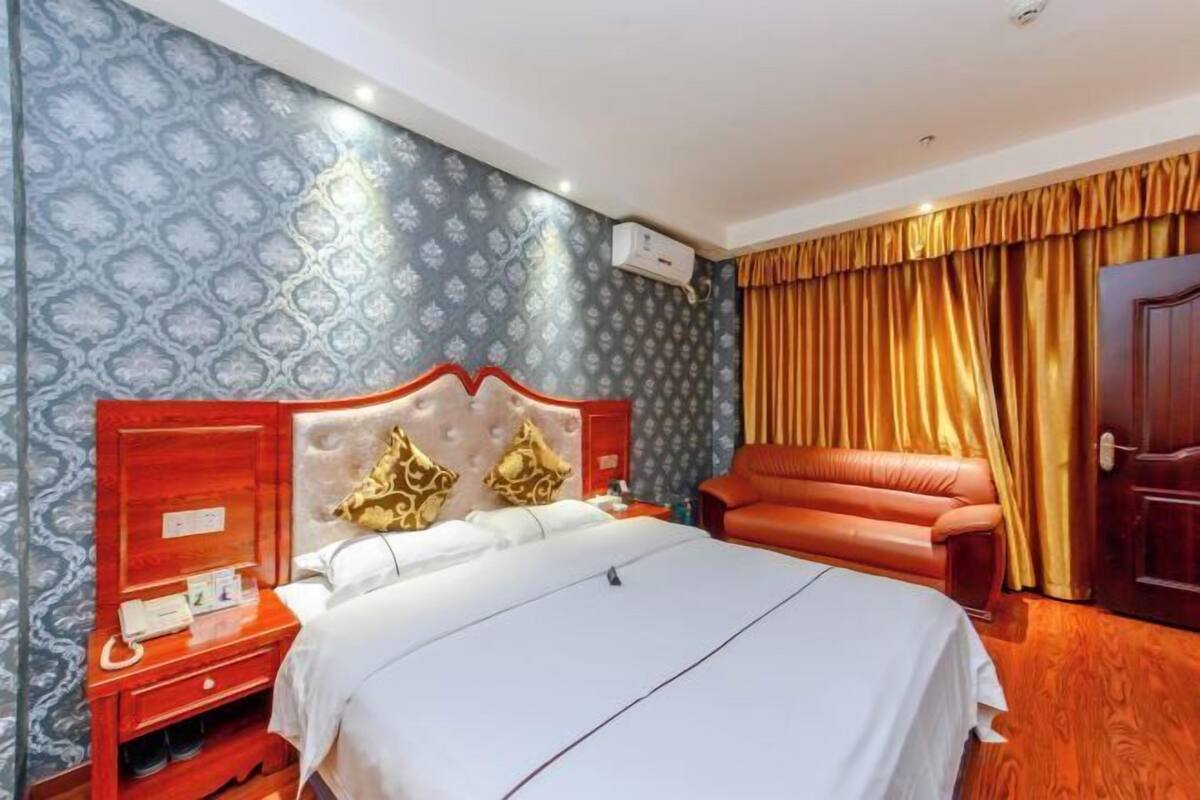 Een hotelkamer met een groot bed, een houten nachtkastje, een rode leren bank en behang met een patroon.