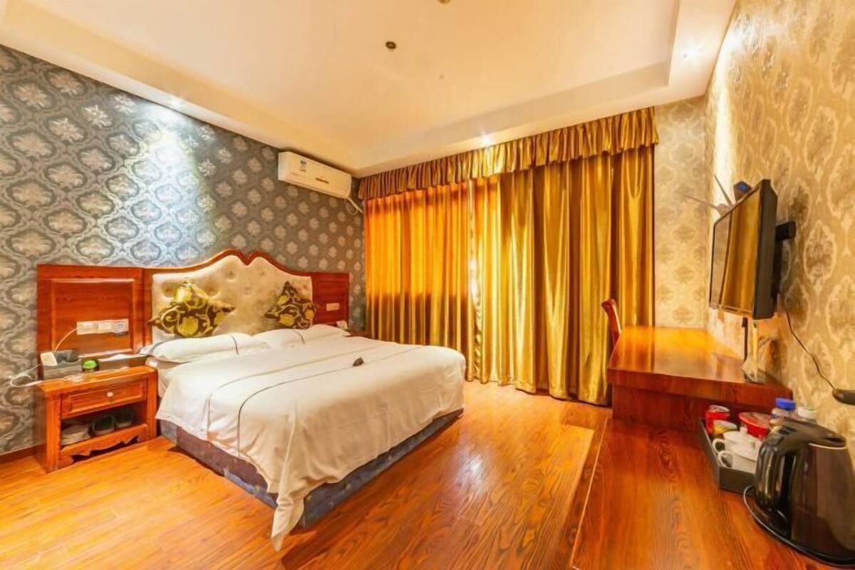 Een hotelkamer met een houten bed, een nachtkastje, een televisie en een raam met gordijnen.