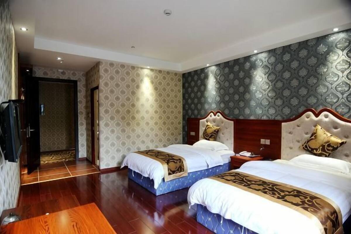 Een hotelkamer met twee bedden, een houten vloer, een kamer met een patroon en een deur naar een gang.