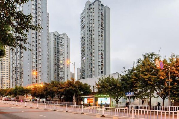A high-rise residential building with multiple floors, surrounded by trees and a white fence.