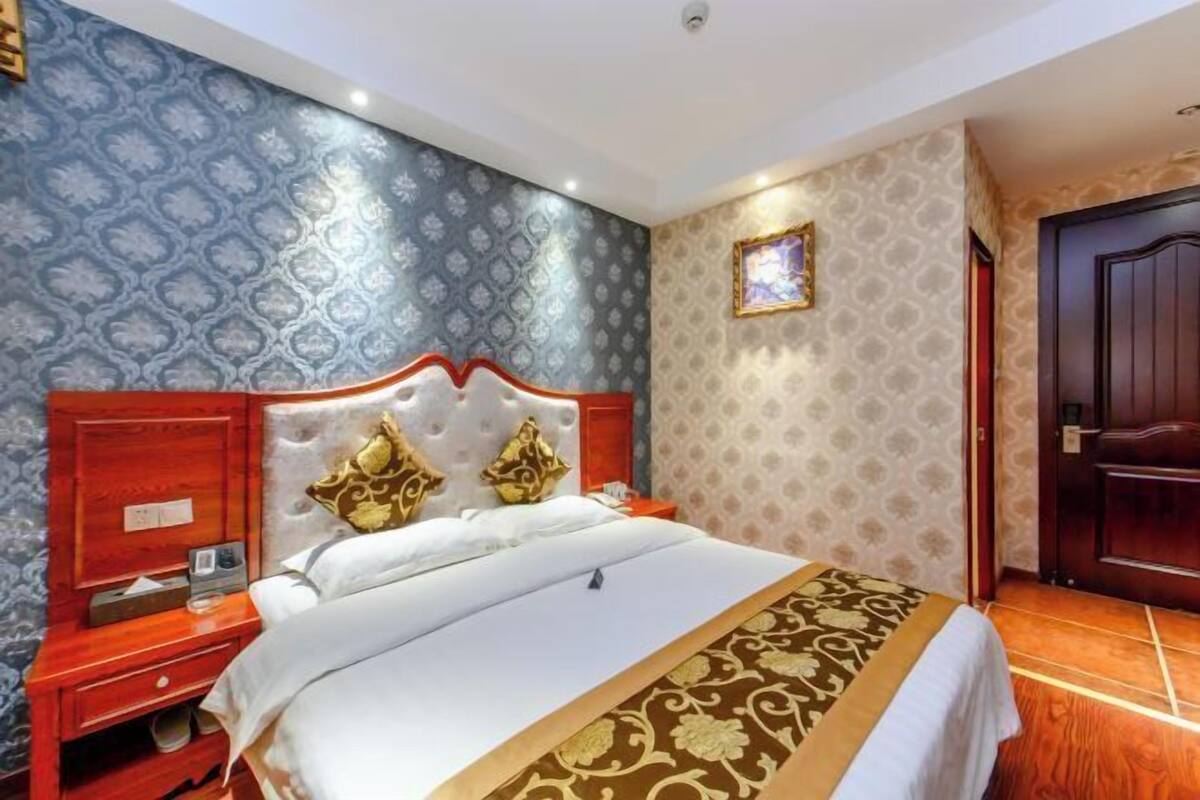 Hotelkamer met een groot bed, een houten nachtkastje, een rode muur en behang met een patroon.