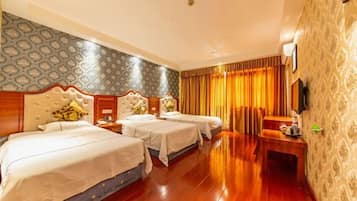 A hotel room with three beds, a wooden floor, patterned wallpaper, and a television on the wall.