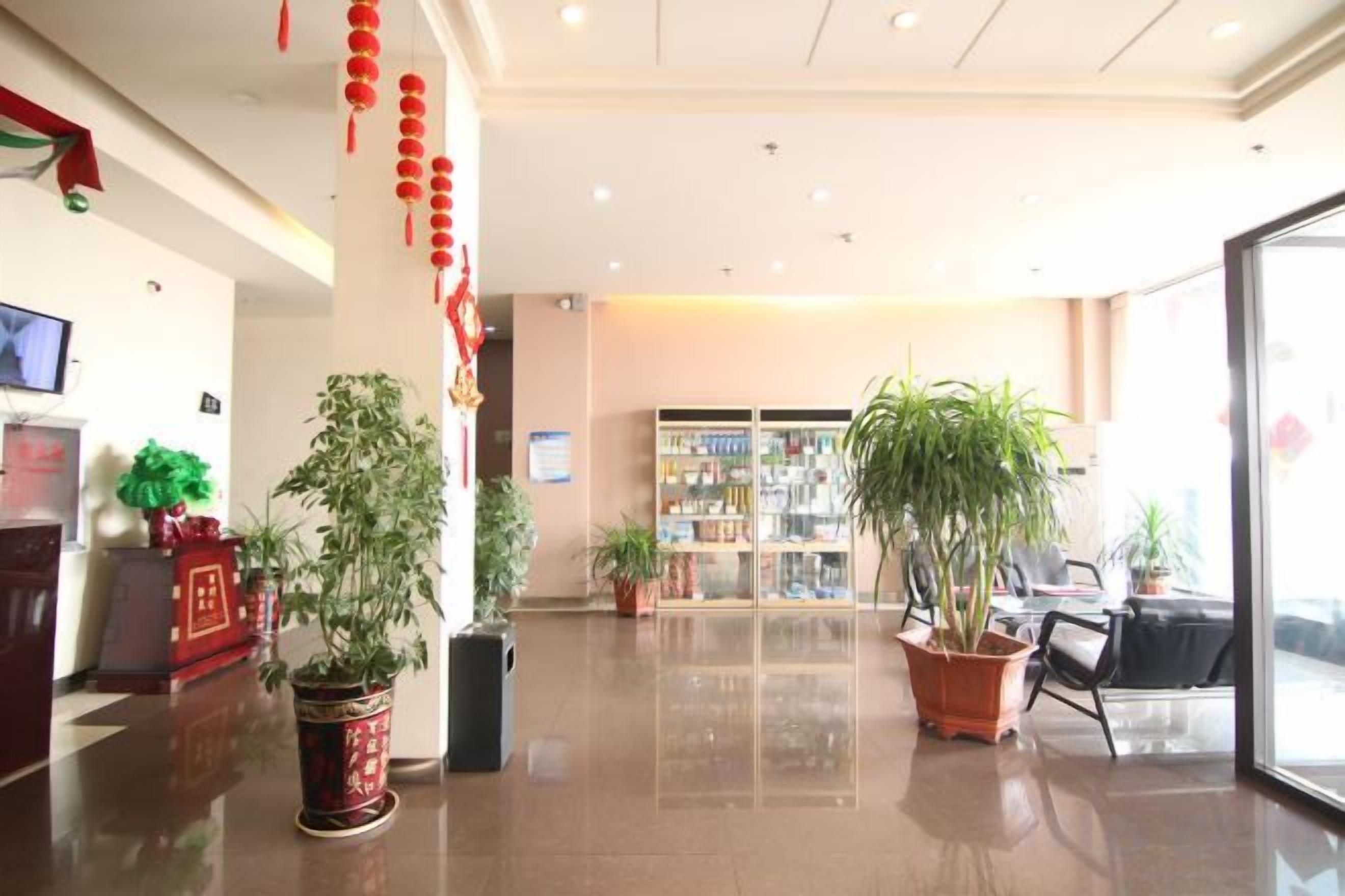 A hotel lobby with a reception desk, potted plants, and a seating area.