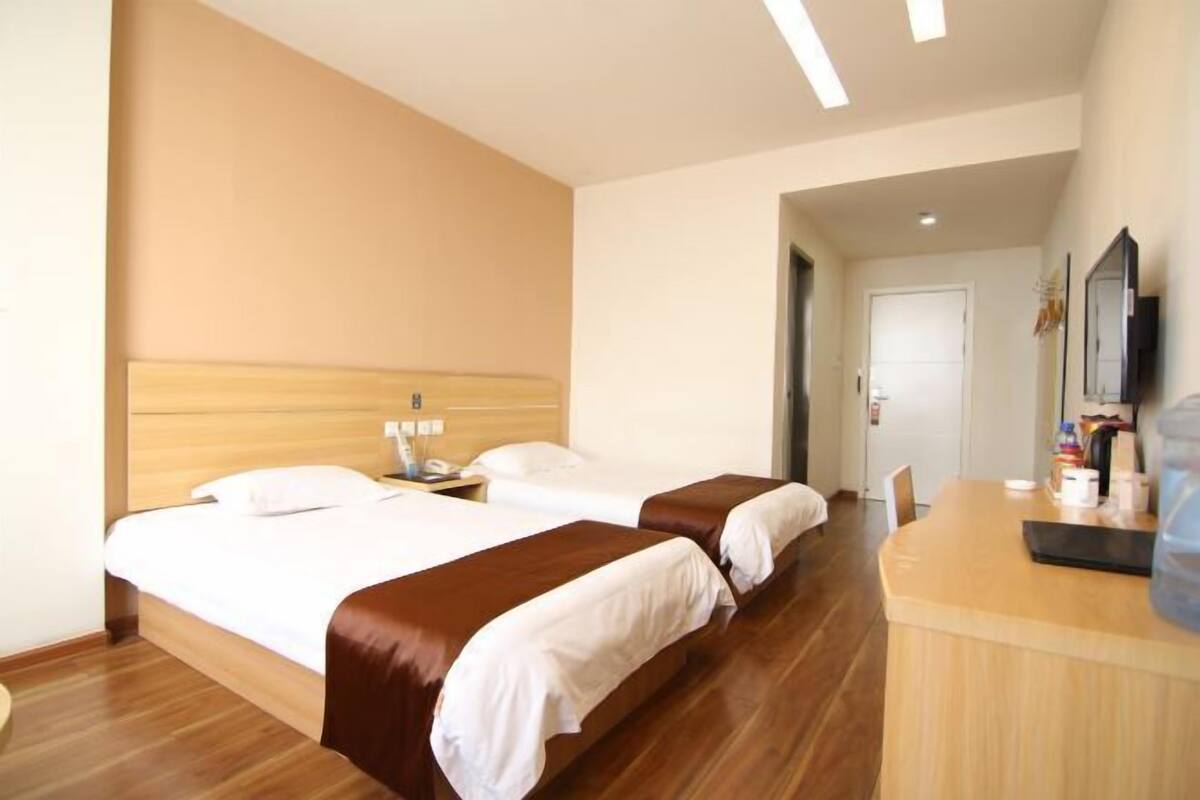 A hotel room with two beds, a wooden headboard, a desk with a chair, and a large mirror.