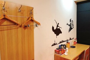 Una habitación con un armario de madera, perchero en la pared, una mesa con cafetera y un adhesivo mural con el horizonte de una ciudad.