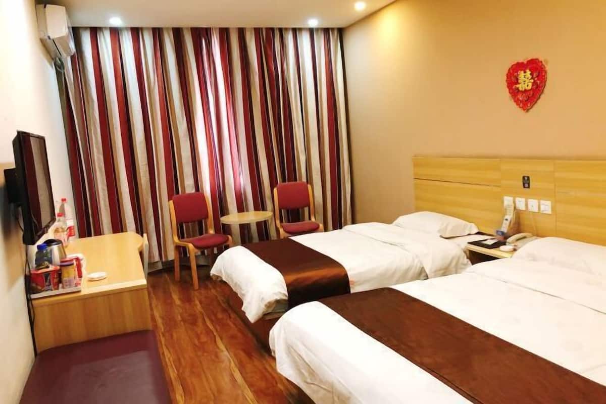 A hotel room with two beds, a small table, a chair, a TV, and a curtain with a red heart decoration.