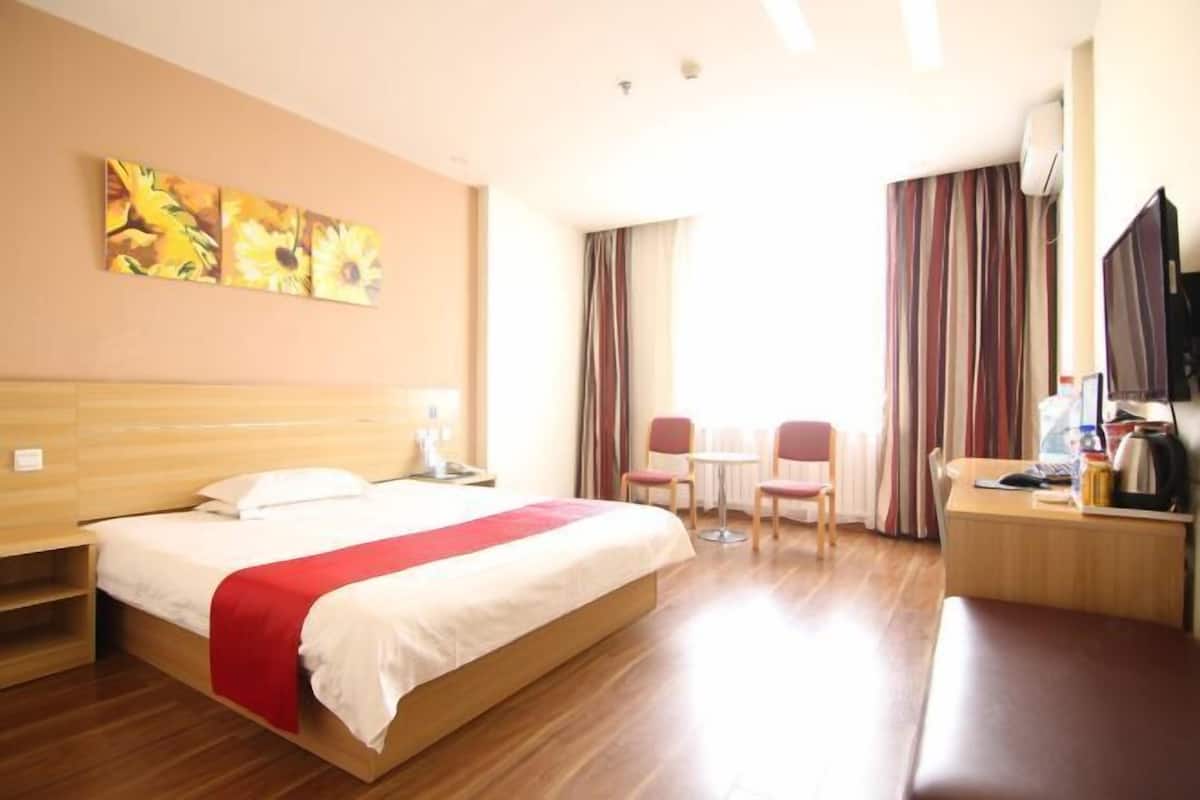 A hotel room with a bed, a desk, a chair, a TV, and a painting on the wall.