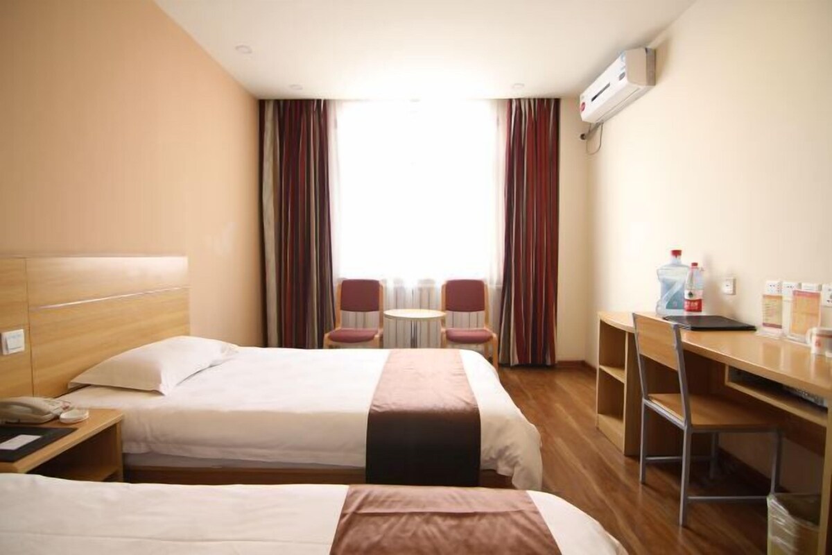 A hotel room with two beds, a desk, a chair, a small table, and a window with curtains.