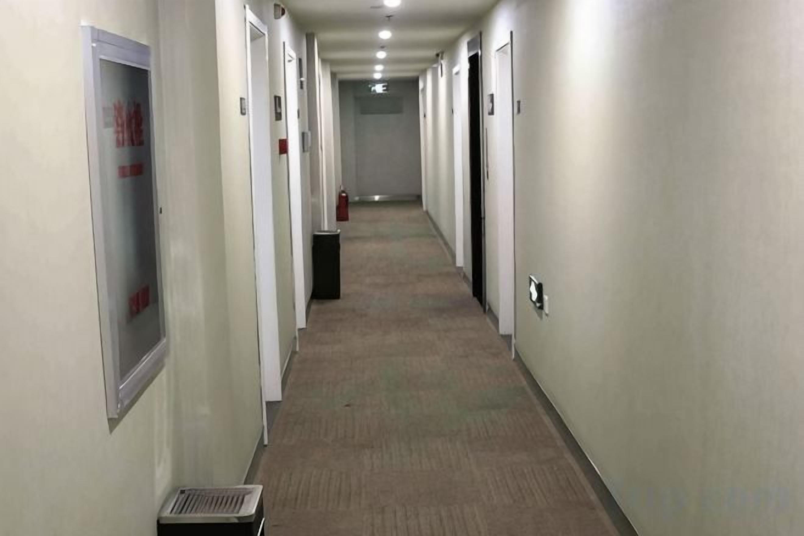 A long, narrow hallway with doors on both sides, a fire extinguisher, and a vent on the left.