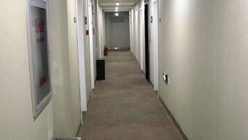A long, narrow hallway with doors on both sides, a fire extinguisher, and a vent on the left.