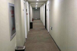 Un pasillo largo y estrecho con puertas a ambos lados, un extintor y una rejilla de ventilación a la izquierda.