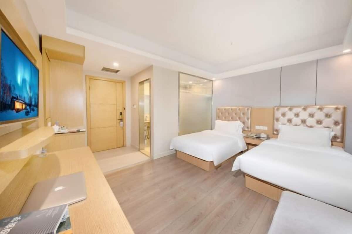 Habitació d'hotel amb dos llits, un escriptori amb un ordinador portàtil, un televisor i una porta de vidre que dona a un bany.