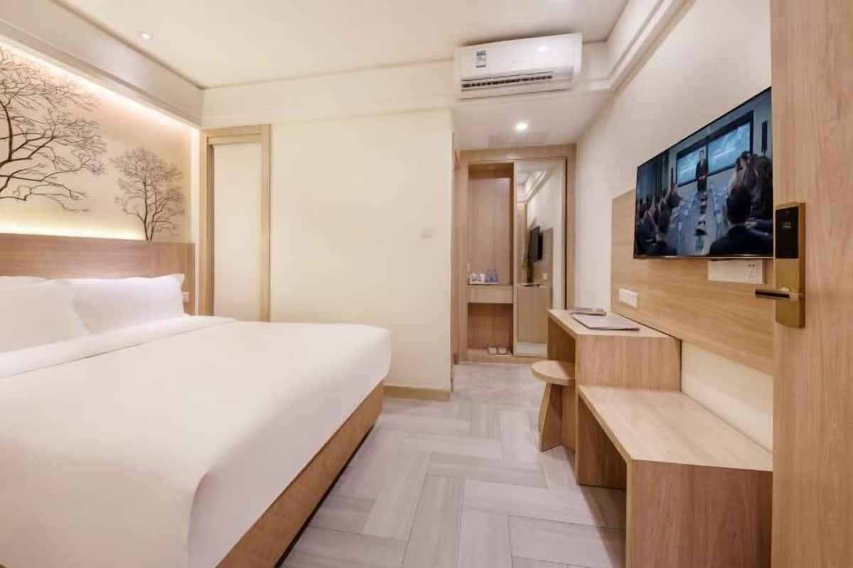 Una habitació d'hotel amb un llit, televisió penjada a la paret, escriptori i mirall.