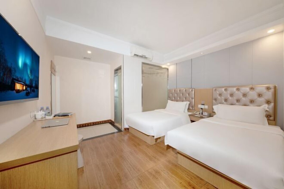 A hotel room with two beds, a desk, a chair, a TV, and a painting.