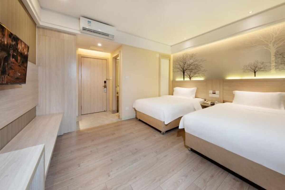 A hotel room with two beds, a wooden floor, a painting on the wall, and a tree mural on the ceiling.