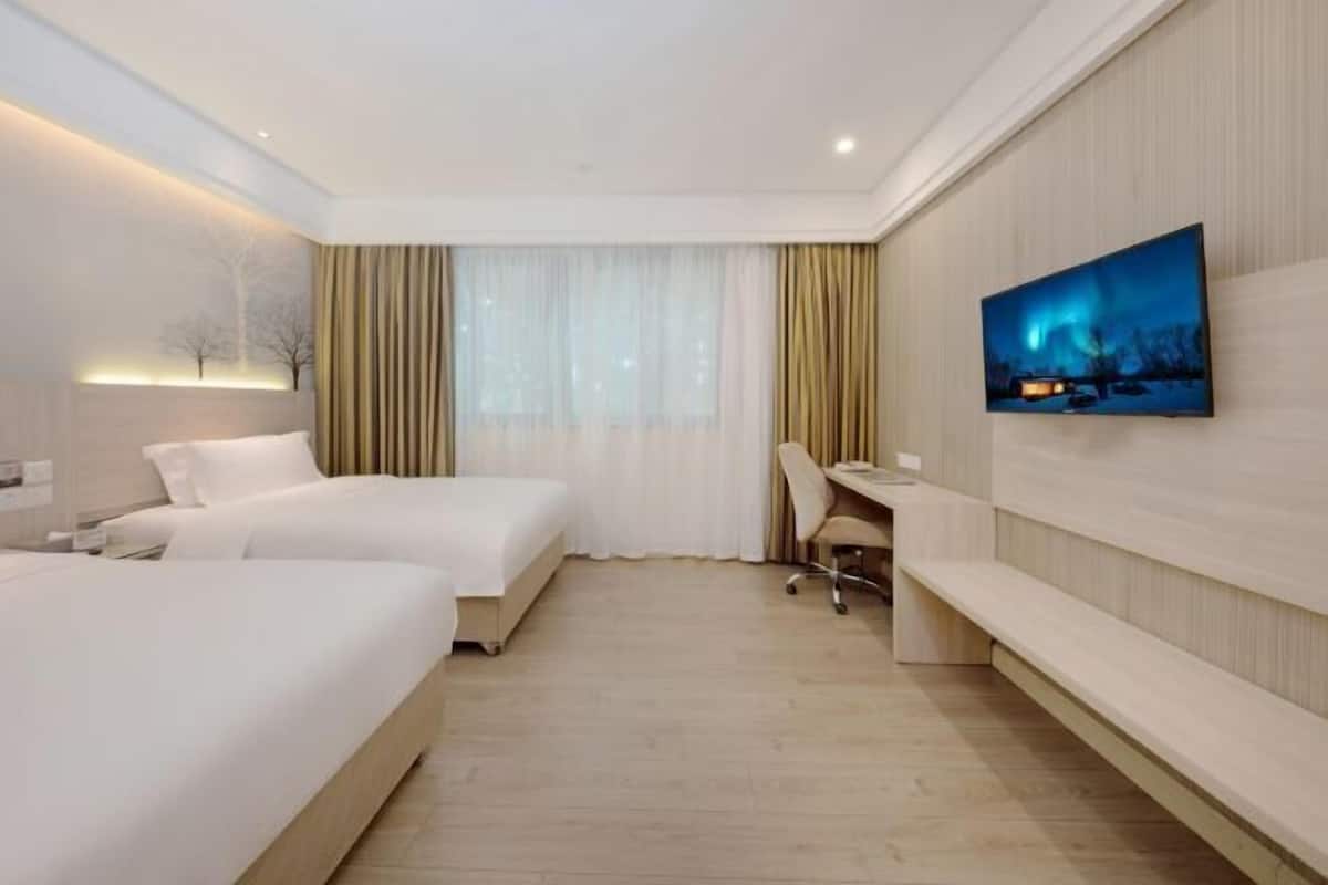 Habitació d'hotel amb dos llits, una taula de treball, una cadira, un televisor i una finestra amb cortines.