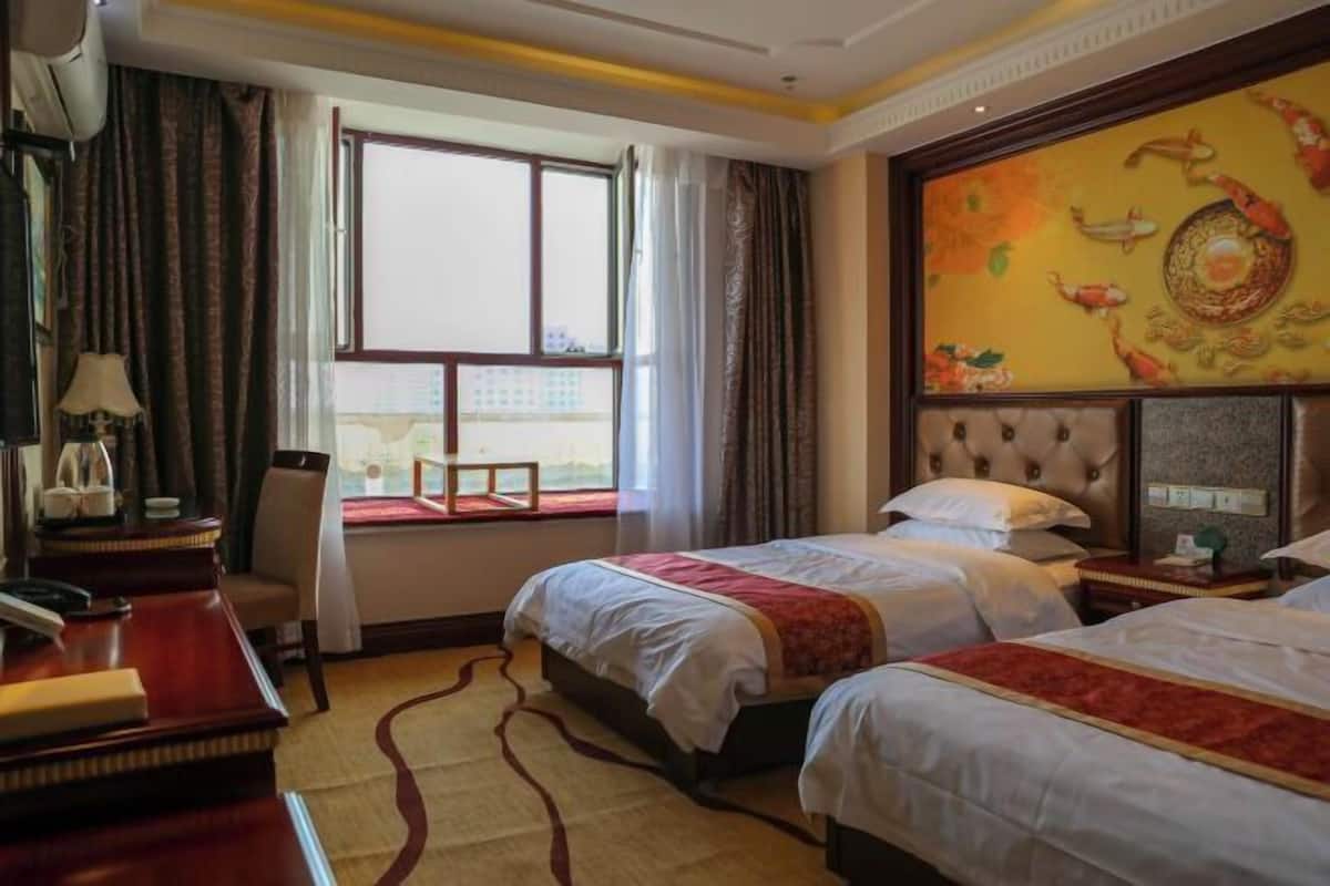 A hotel room with two beds, a desk, a chair, a window with curtains, and a decorative wall painting.