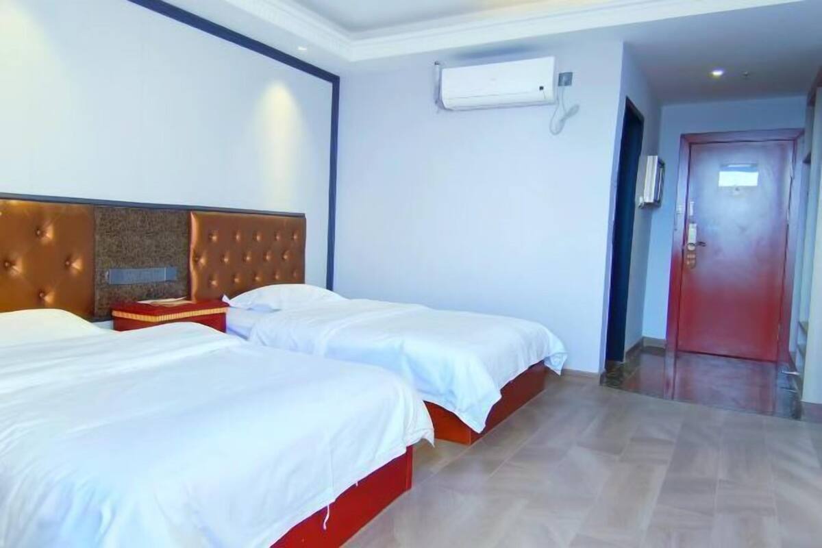 A hotel room with two beds, a red headboard, a white wall, and a door.
