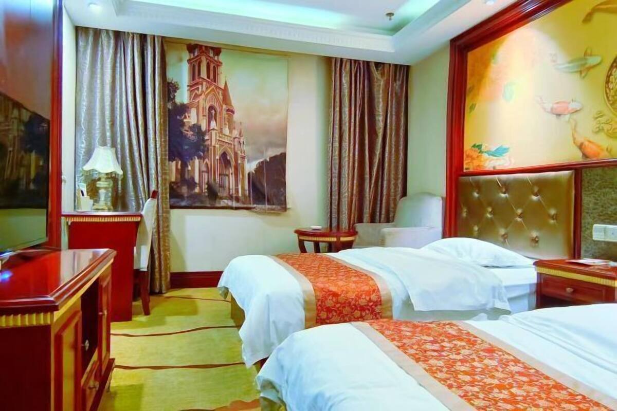 A hotel room with two beds, a wooden dresser, a desk, a chair, and a large painting on the wall.