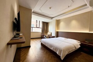 A hotel room with a bed, a desk with a chair, a television, and a window with curtains.