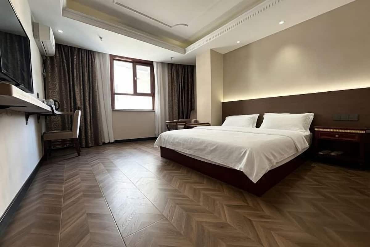 A hotel room with a large bed, a desk, a chair, a TV, and a window with curtains.