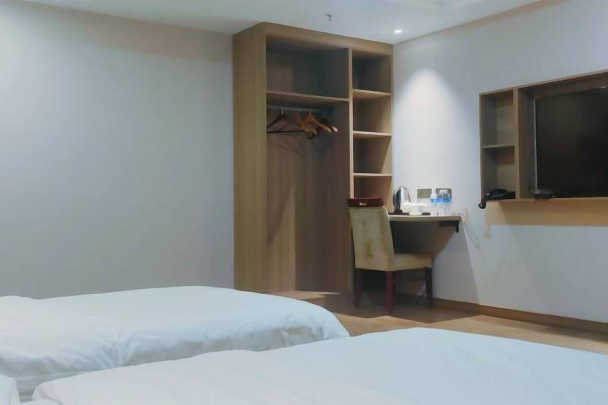 A hotel room with two beds, a desk with a chair, a wardrobe, and a TV mounted on the wall.