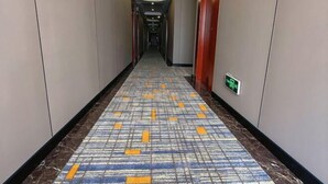 A hotel hallway with patterned carpet, a visible exit sign, and a door on the right. - Klamar Law Rode Hotel (Karamay)
