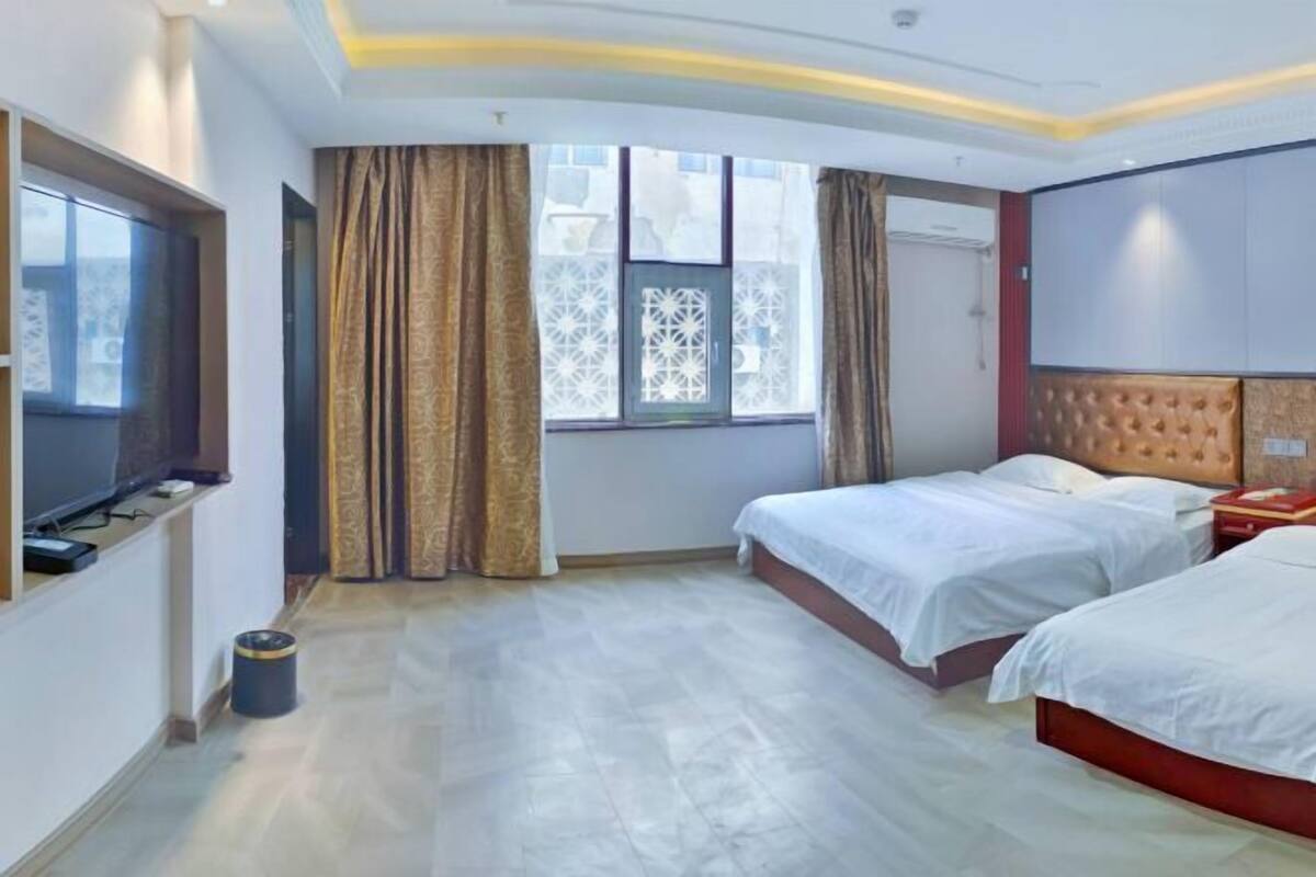 A hotel room with two beds, a TV, a desk, and a window with curtains.