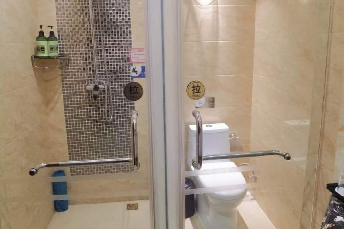 A bathroom with a glass door, a shower with a tiled wall, a toilet, and a handrail.
