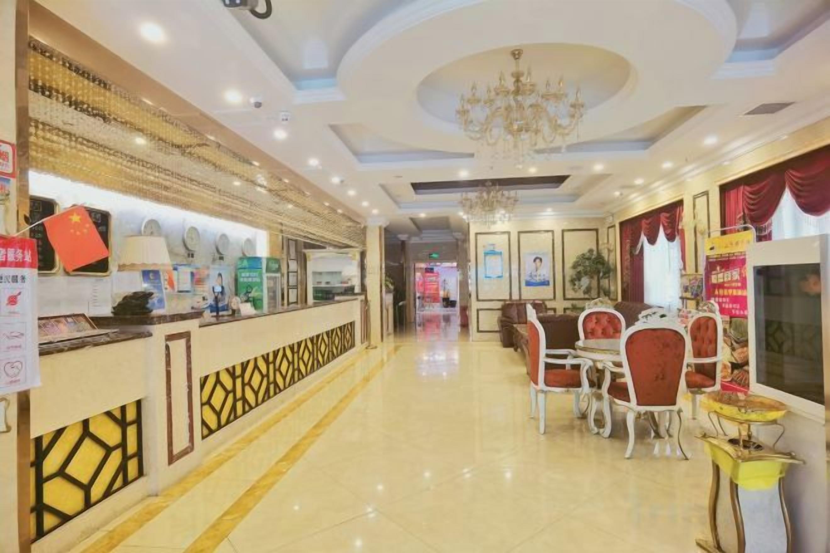 A hotel lobby with a reception desk, dining area with chairs and tables, and a chandelier.