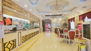 A hotel lobby with a reception desk, dining area with chairs and tables, and a chandelier.