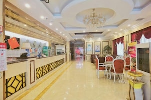 A hotel lobby with a reception desk, dining area with chairs and tables, and a chandelier.