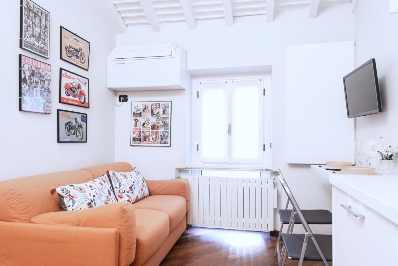 A modern living room with a sofa, a radiator, a window, and a TV mounted on the wall.