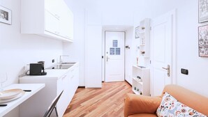A modern kitchen with white cabinets, a coffee machine, and a dining area with a table and chairs. - Easylife - Delicious Studio in Brera/Duomo (Milano)