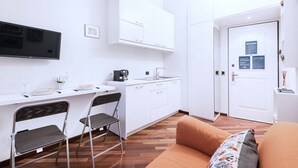 A compact living space with a kitchenette, a dining area with chairs, a sofa, and a flat-screen TV mounted on the wall. - Easylife - Delicious Studio in Brera/Duomo (Milano)