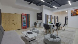 A modern hostel room with wooden lockers, a Coca-Cola fridge, a Pro Hostel sign, a dining area with tables and chairs, and a cozy seating area with bean bags. - Hostel Pro (Bishkek)