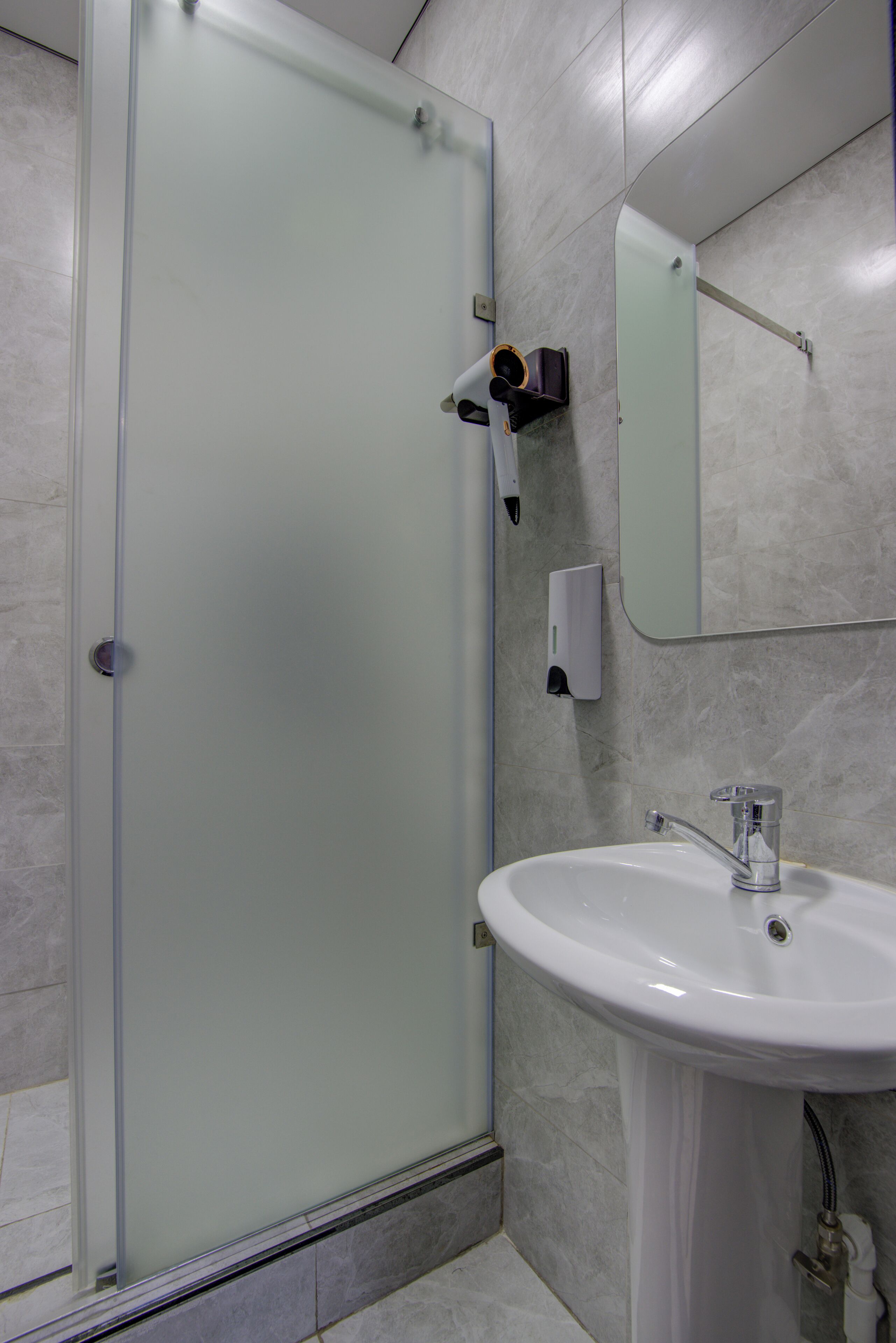 Een badkamer met een douchecabine van glas, een witte wastafel en een spiegel boven de wastafel.