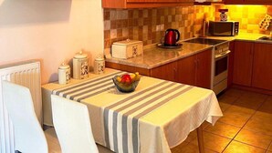 A compact kitchen with wooden cabinets, a microwave, a kettle, and a dining area with a striped tablecloth. - SV Apartment with sea view (Corfu)