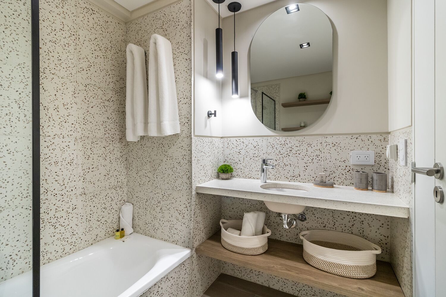 Ein modernes Badezimmer mit einer freistehenden Badewanne, einem großen Spiegel und einem weißen Waschtisch mit Spüle und Aufbewahrungskörben.