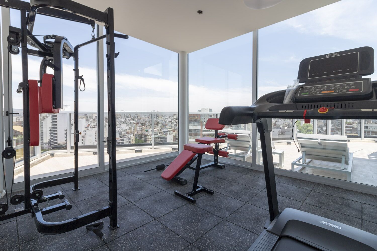 Un gimnasio con equipo de ejercicio, ventanas amplias y vistas a la ciudad.