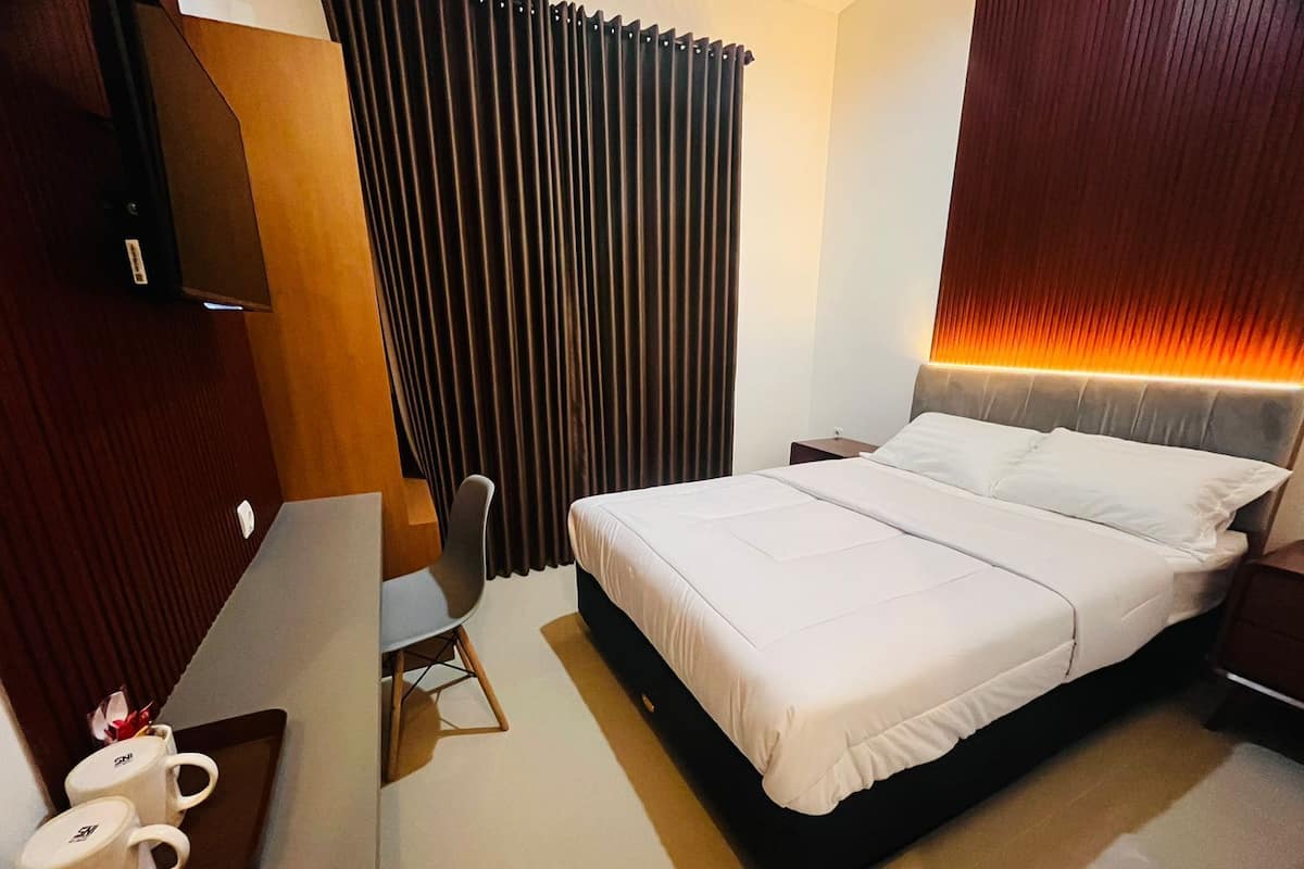 Habitación de hotel con cama, escritorio con silla, televisor y ventana con cortinas.