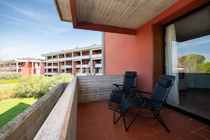 A balcony with two chairs and a table, overlooking a building with multiple balconies. - Little Flower (Desenzano del Garda)