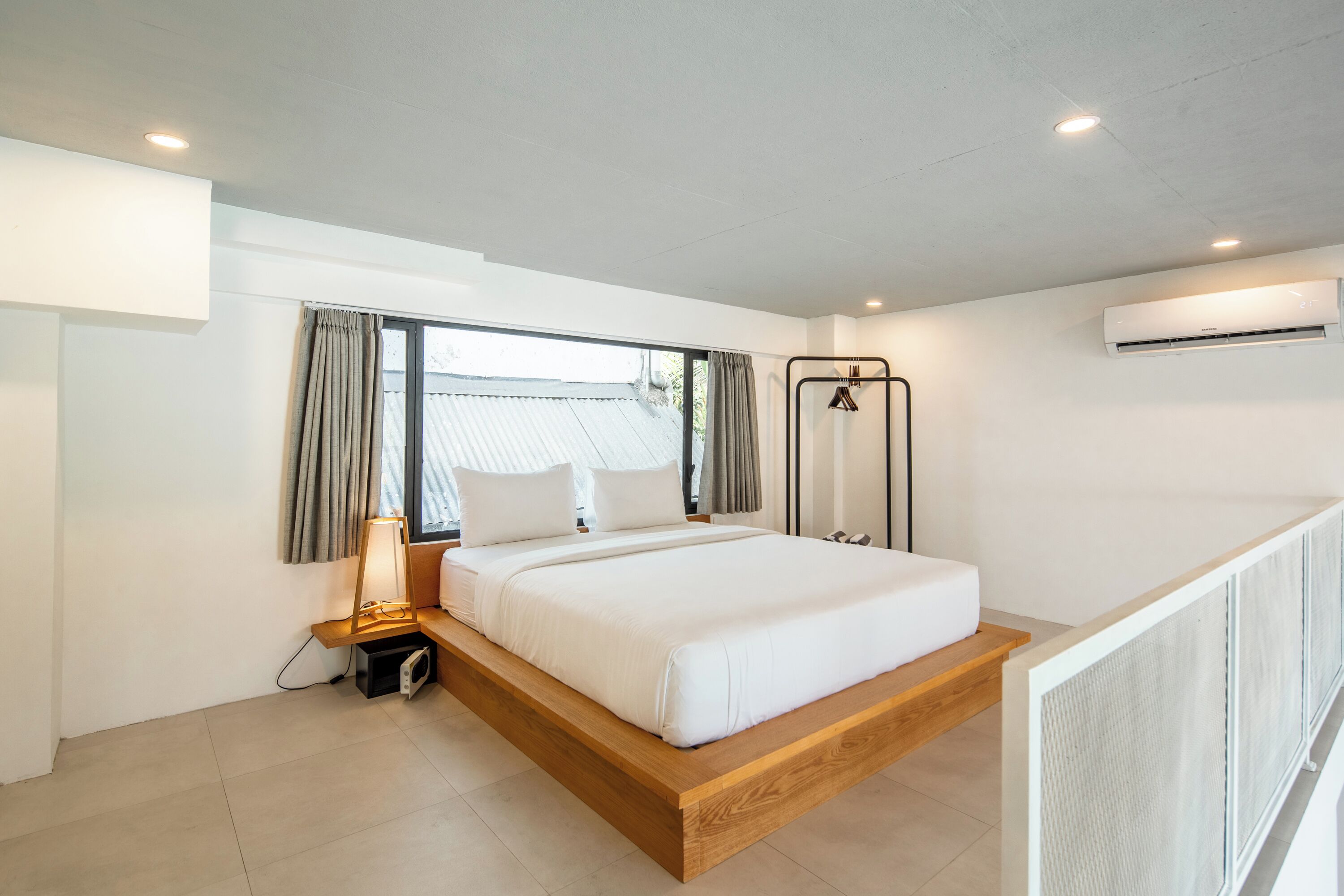A modern bedroom with a wooden platform bed, a bedside lamp, and an air conditioning unit.
