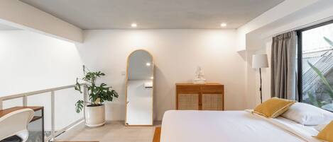 A modern bedroom with a large bed, a desk, a potted plant, a mirror, and a wardrobe.