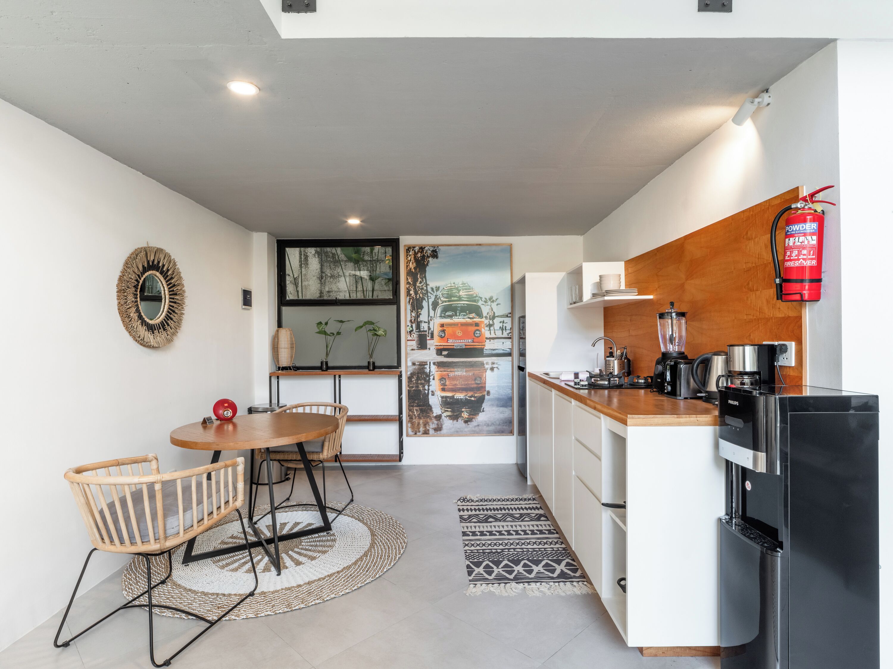 A modern kitchen with a dining area, featuring a round table, chairs, a coffee machine, and a refrigerator.