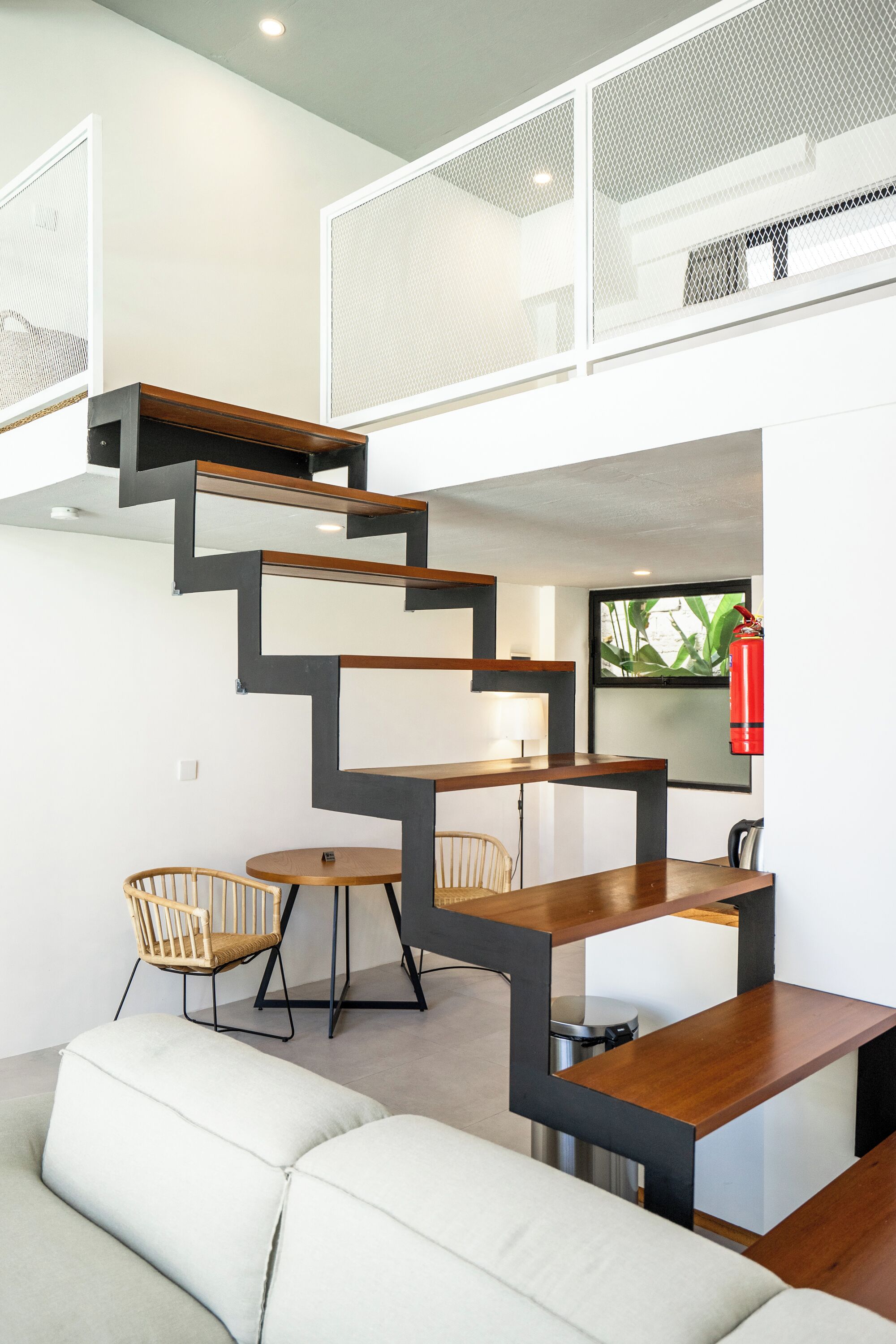 Un interior moderno con una escalera que conduce a un nivel superior, un comedor con mesa y sillas, y un sofá.