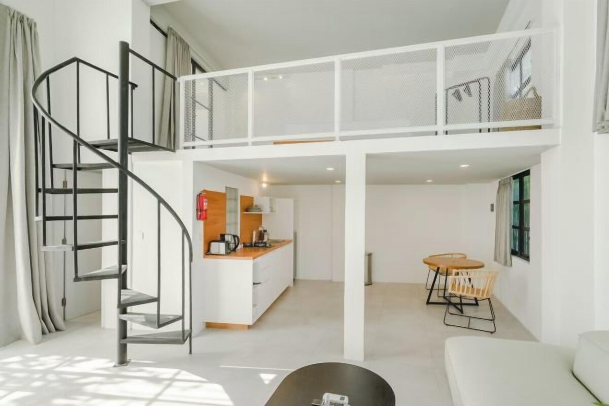 A modern interior with a spiral staircase, a kitchen area, a dining table, and a sofa.