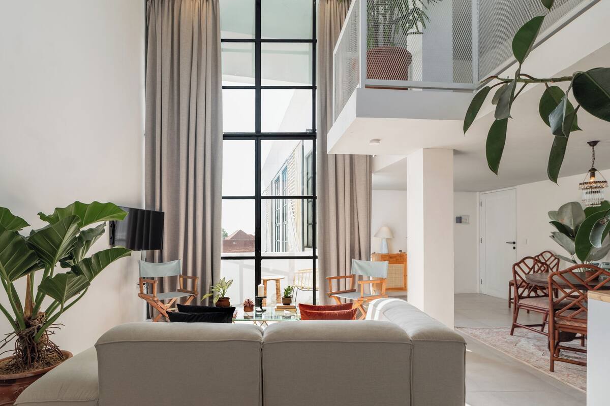 Een moderne woonkamer met een groot raam, een bank, een eethoek en een balkon met planten.